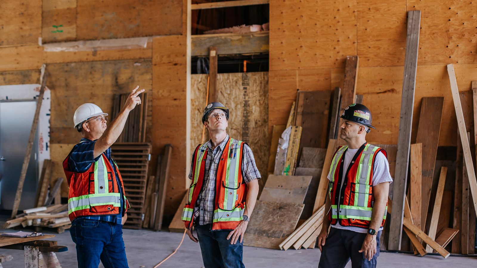 Three Kelco Drywall employees in safety hats and vests as they inspect a drywall installation job by Kelco Drywall.
